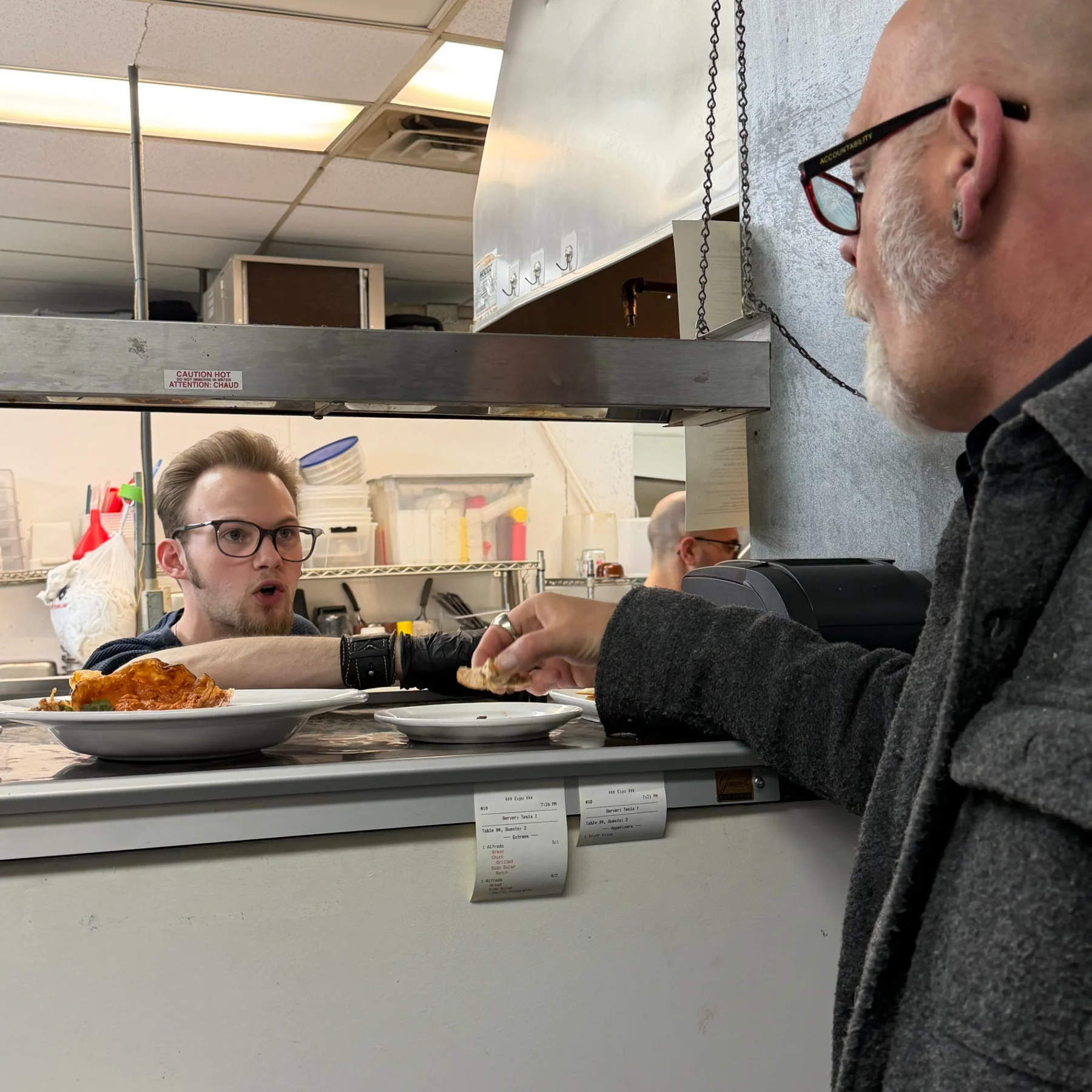 A conversation across the restaurant kitchen pass, with the head chef on the kitchen side.